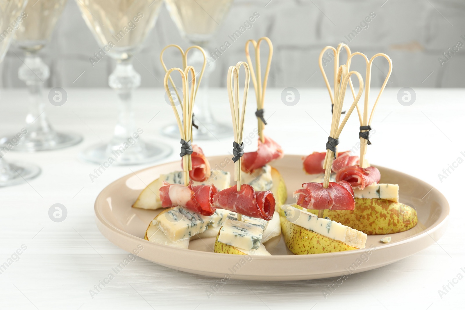 Photo of Tasty canapes with pears, blue cheese and prosciutto on white wooden table, closeup