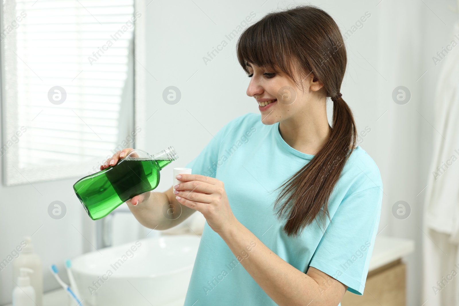 Photo of Young woman using mouthwash in bathroom. Oral hygiene