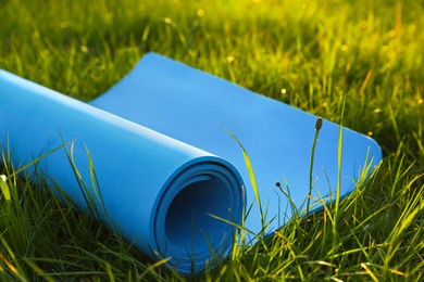 Photo of Blue karemat or fitness mat in fresh green grass outdoors, closeup