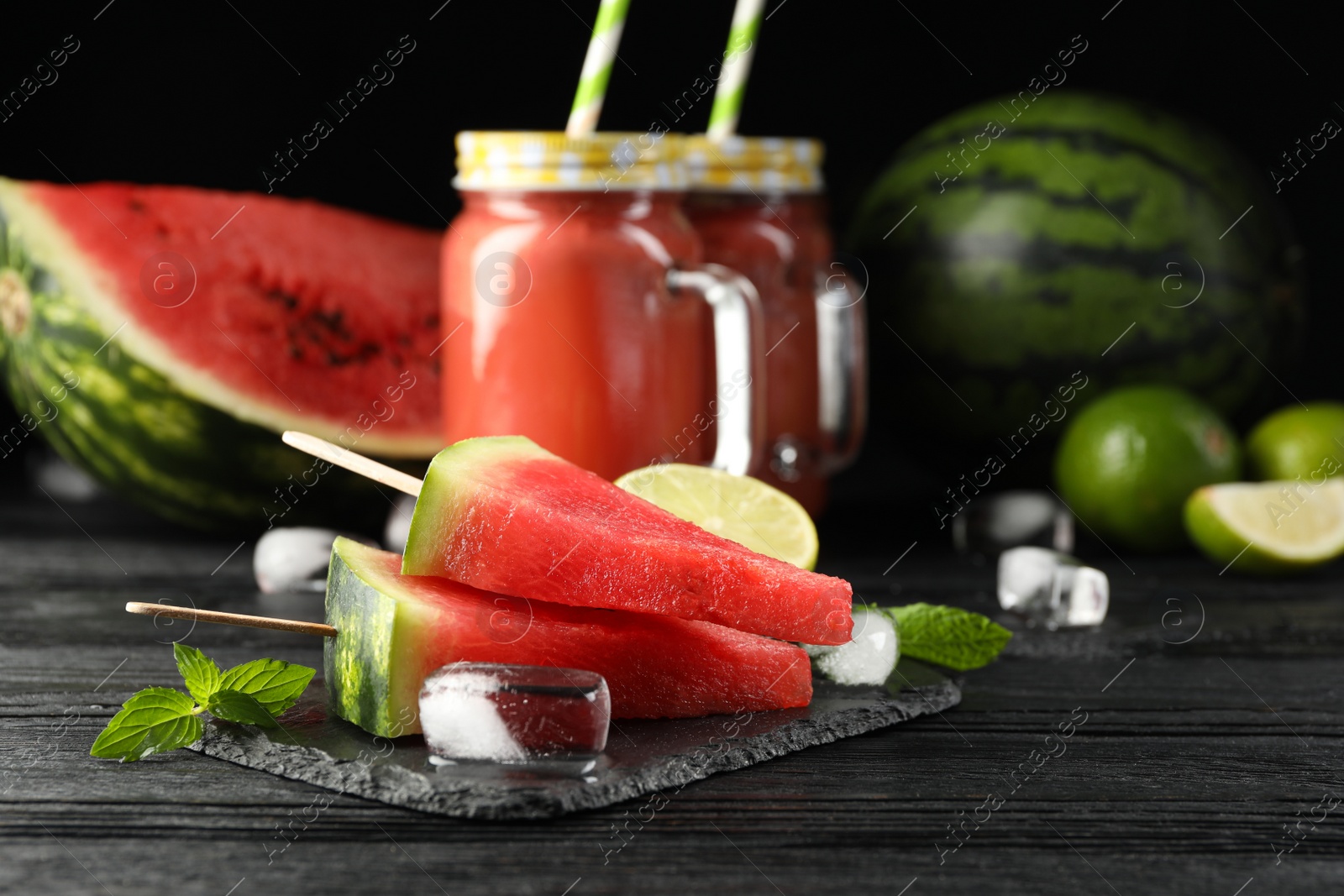 Photo of Slate board with juicy watermelon, ice and lime on black wooden table