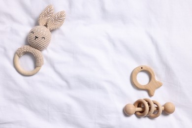 Photo of Baby accessories. Teethers and rattle on white fabric, flat lay. Space for text