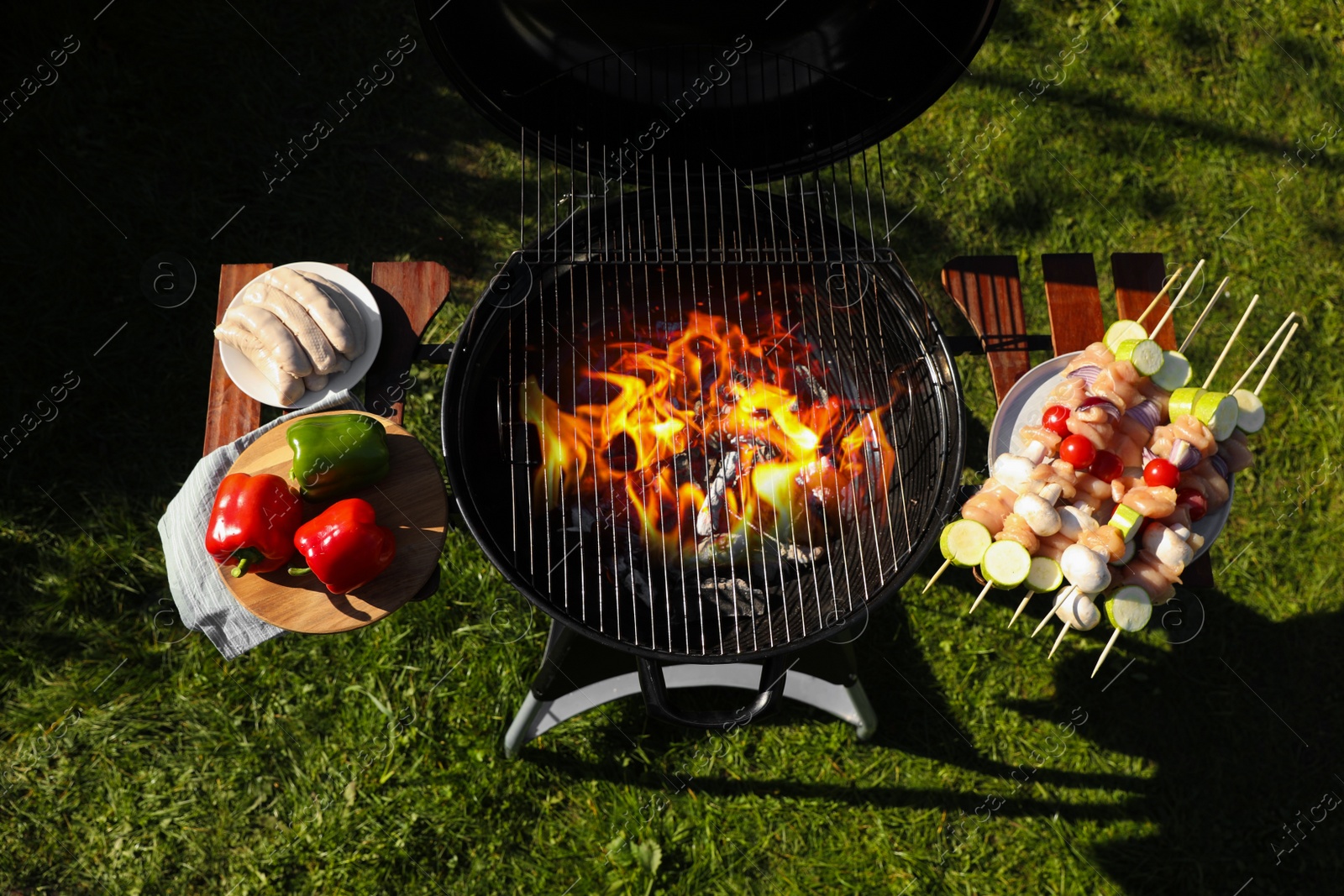 Photo of Skewers with meat and vegetables near barbecue grill outdoors, top view