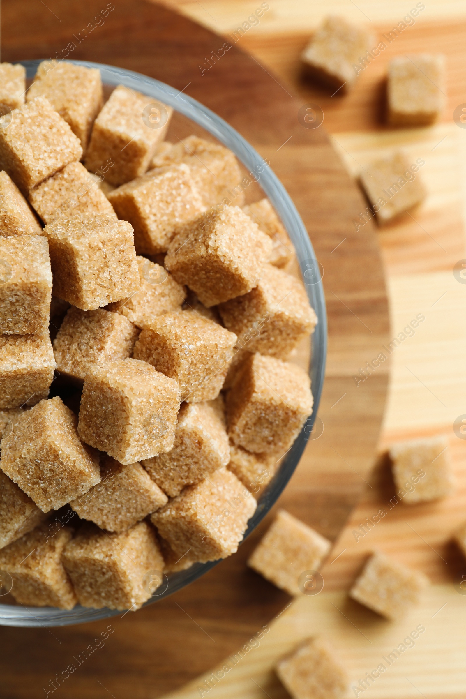 Photo of Brown sugar cubes in bowl on wooden table, top view