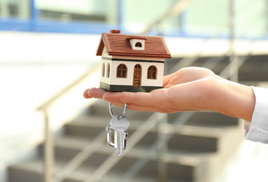 Real estate agent holding key and house model outdoors, closeup