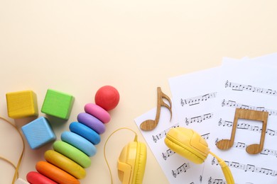 Wooden notes, music sheets, headphones and toys on beige background, flat lay with space for text. Baby song concept