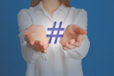 Image of Hashtag concept. Woman holding sign on light blue background, closeup