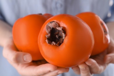 Photo of Woman holding delicious ripe juicy persimmons, closeup