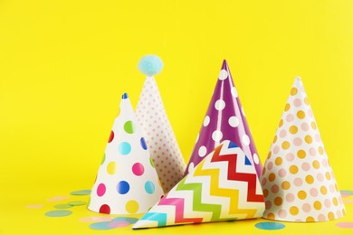 Photo of Bright party hats and confetti on yellow background