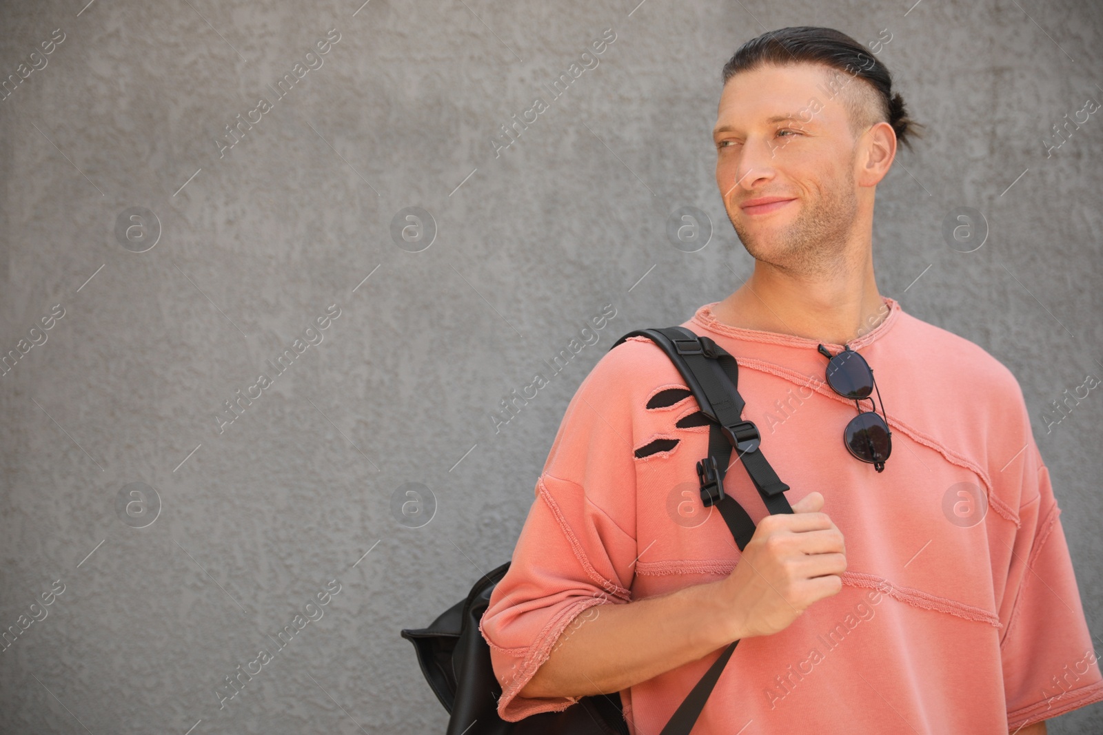 Photo of Handsome young man with stylish sunglasses and backpack near grey wall, space for text