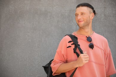 Photo of Handsome young man with stylish sunglasses and backpack near grey wall, space for text