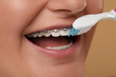 Photo of Woman with dental braces cleaning teeth on brown background, closeup