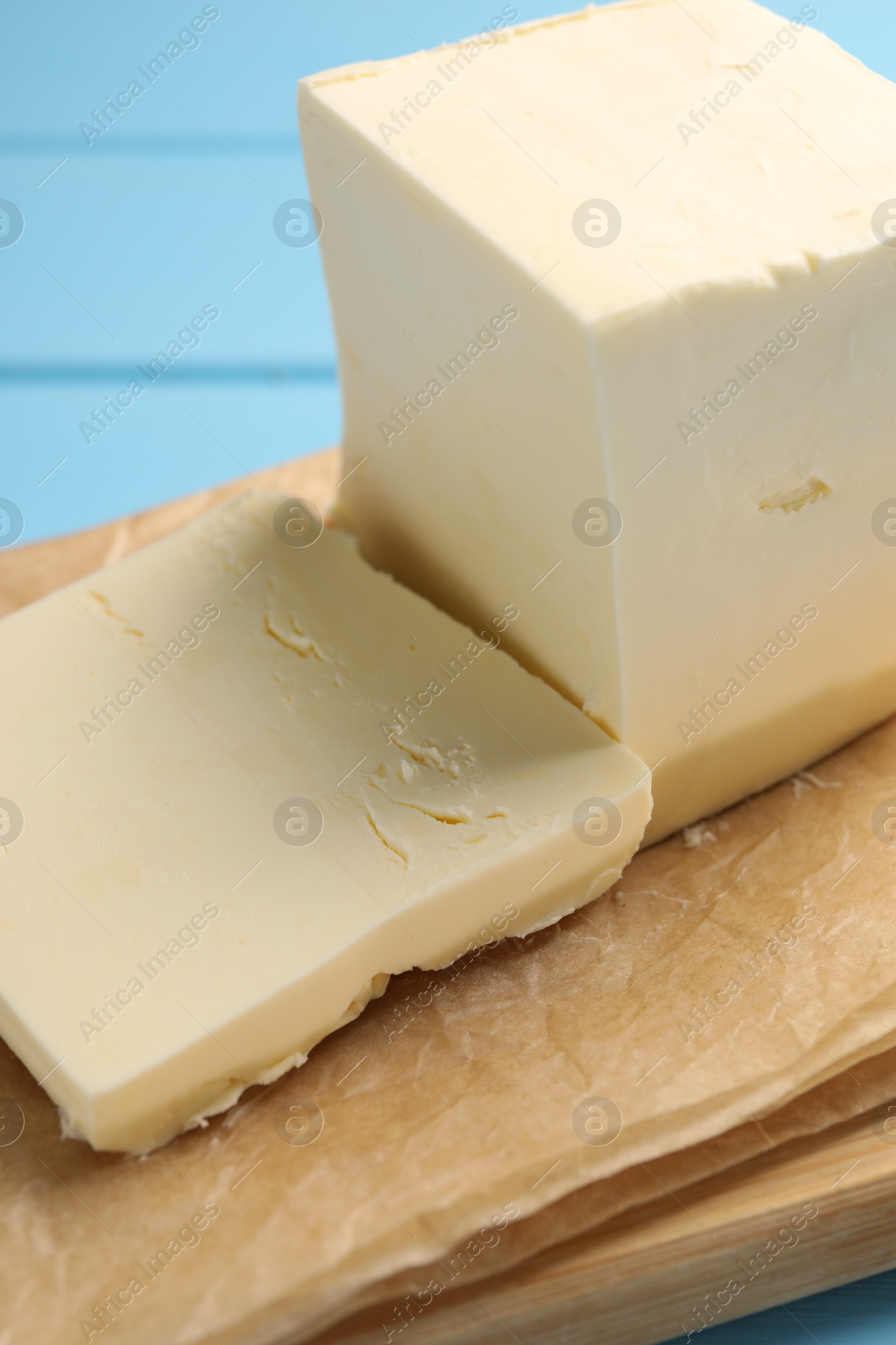 Photo of Block of tasty butter on light blue wooden table, closeup