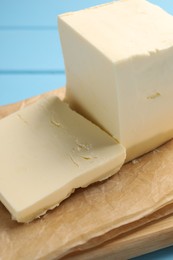 Photo of Block of tasty butter on light blue wooden table, closeup