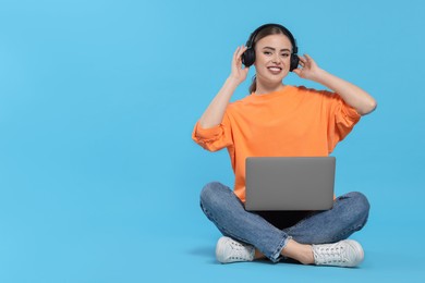 Photo of Happy woman with laptop listening to music in headphones on light blue background. Space for text