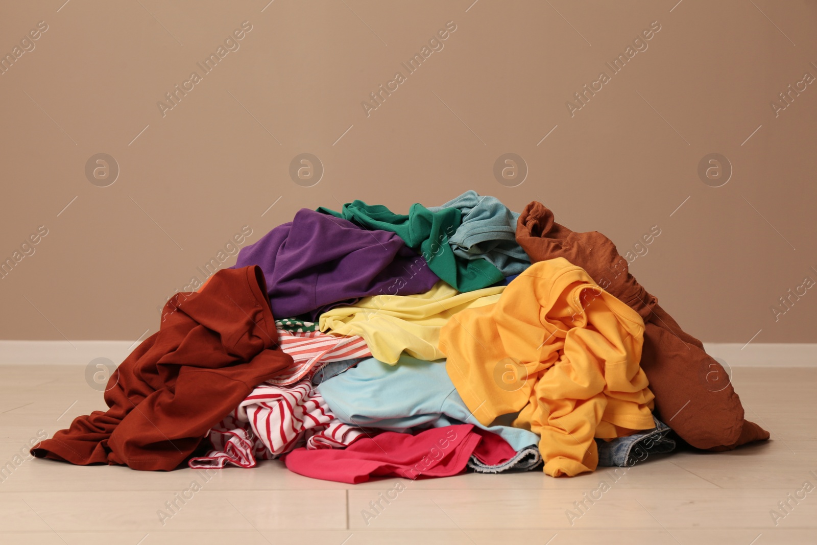 Photo of Pile of dirty clothes on floor near light brown wall indoors