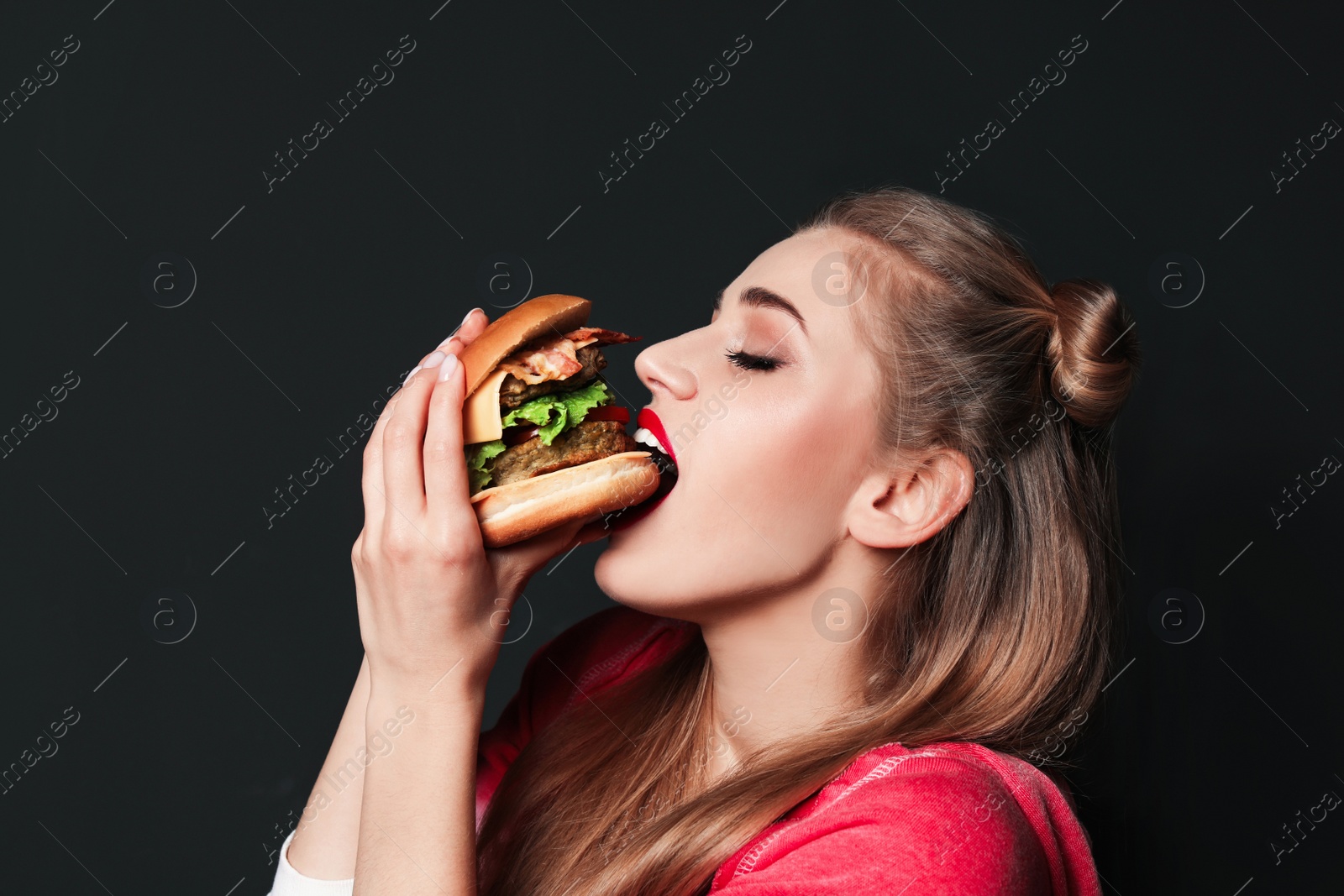 Photo of Pretty woman eating tasty burger on black background