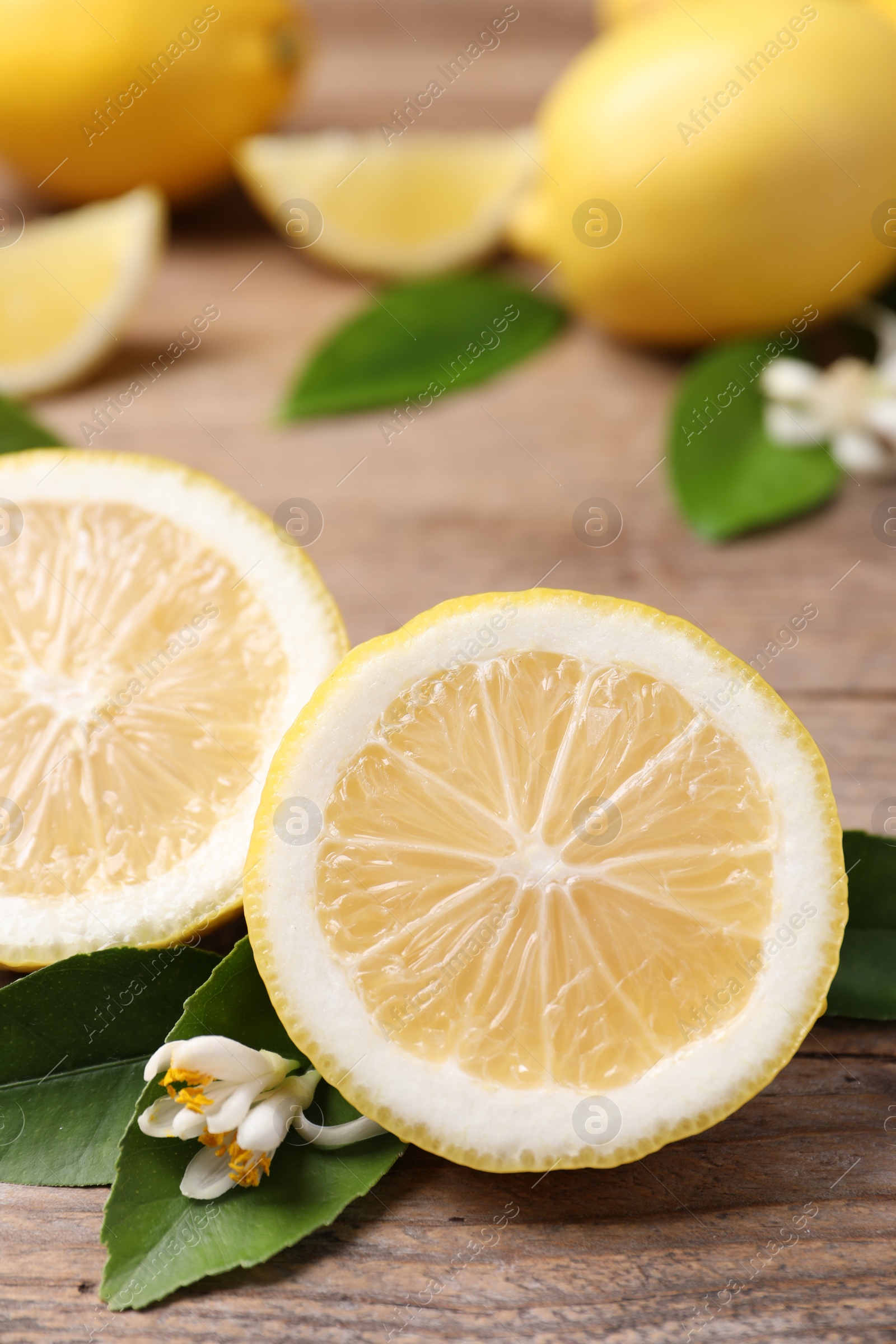 Photo of Many fresh ripe lemons with green leaves and flowers on wooden table, closeup