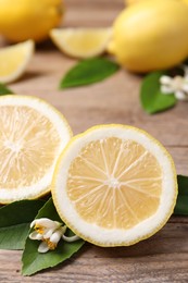 Many fresh ripe lemons with green leaves and flowers on wooden table, closeup