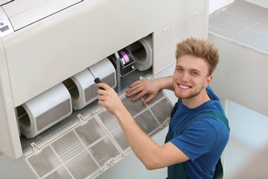 Professional technician maintaining modern air conditioner indoors