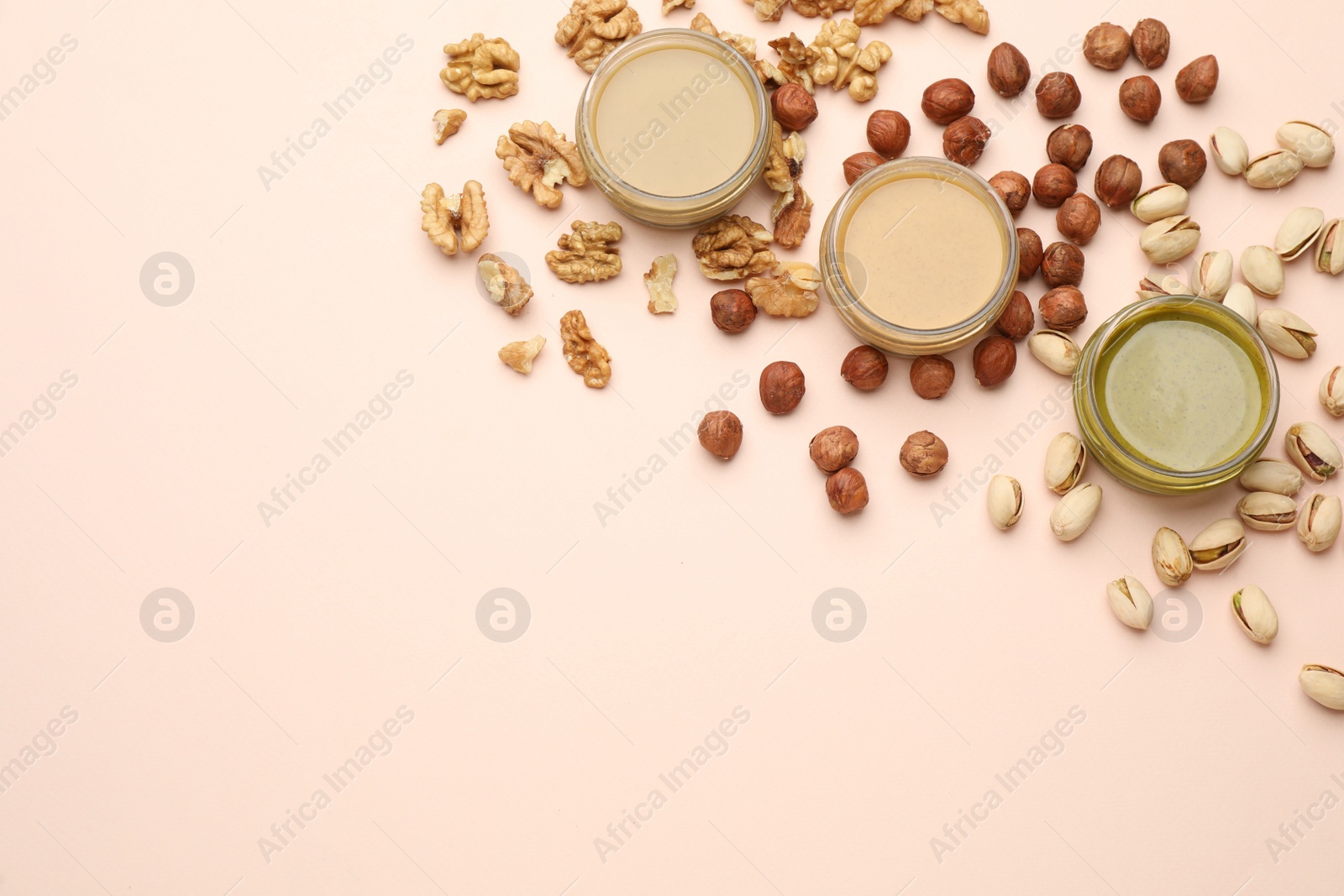 Photo of Different types of delicious nut butters and ingredients on beige background, flat lay. Space for text