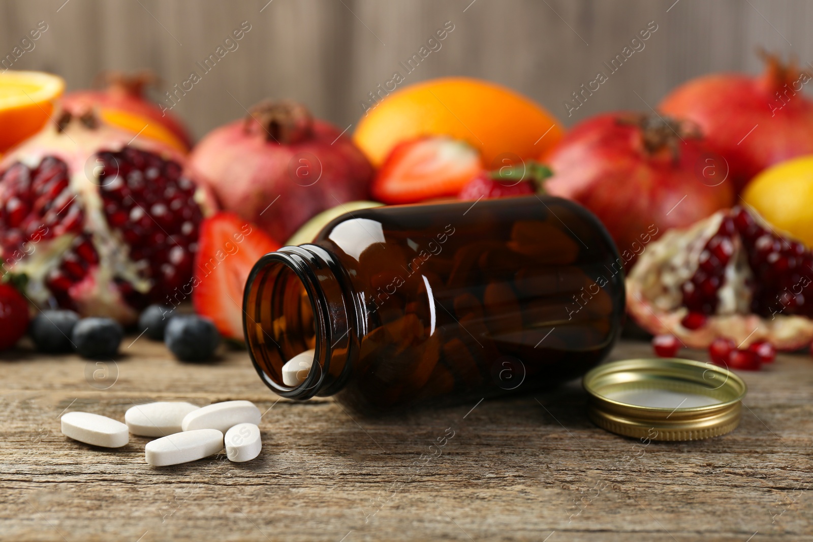 Photo of Vitamin pills, bottle and fresh fruits on wooden table