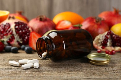 Vitamin pills, bottle and fresh fruits on wooden table