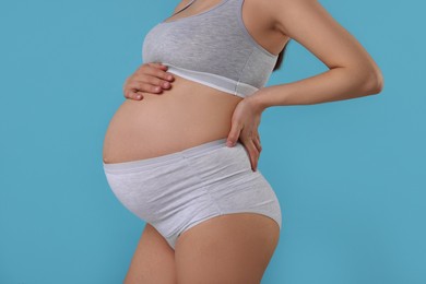 Photo of Pregnant woman in comfortable maternity underwear on light blue background, closeup