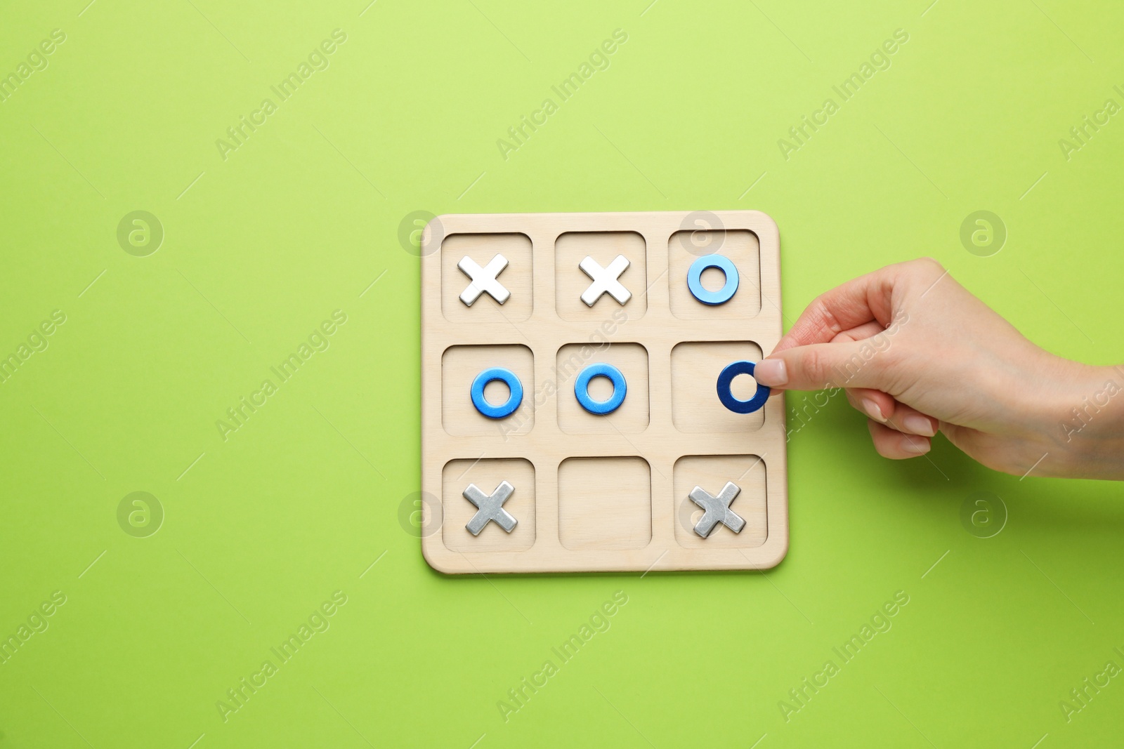 Photo of Woman playing tic tac toe game on light green background, top view