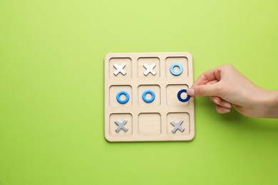 Photo of Woman playing tic tac toe game on light green background, top view