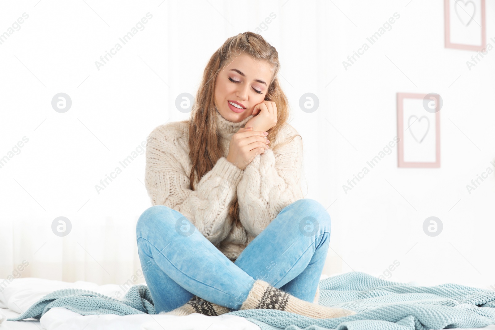 Photo of Beautiful smiling young woman in cozy warm sweater sitting on bed at home