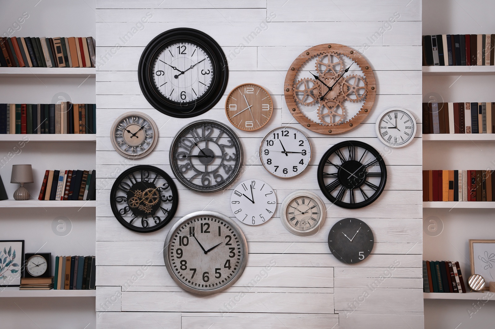 Photo of Collection of different clocks between bookshelves in room. Interior design