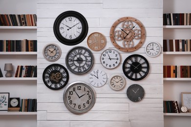 Photo of Collection of different clocks between bookshelves in room. Interior design