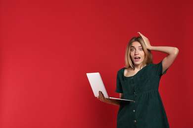 Portrait of emotional woman with modern laptop on red background. Space for text