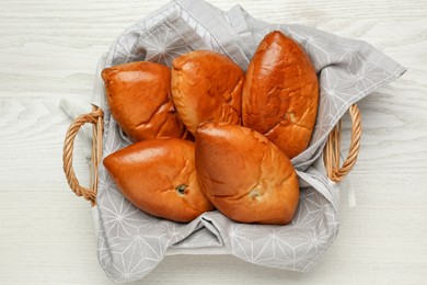 Photo of Wicker basket with delicious baked patties on white wooden table, top view