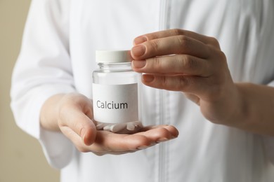 Photo of Calcium supplement. Doctor holding bottle with pills on beige background, closeup