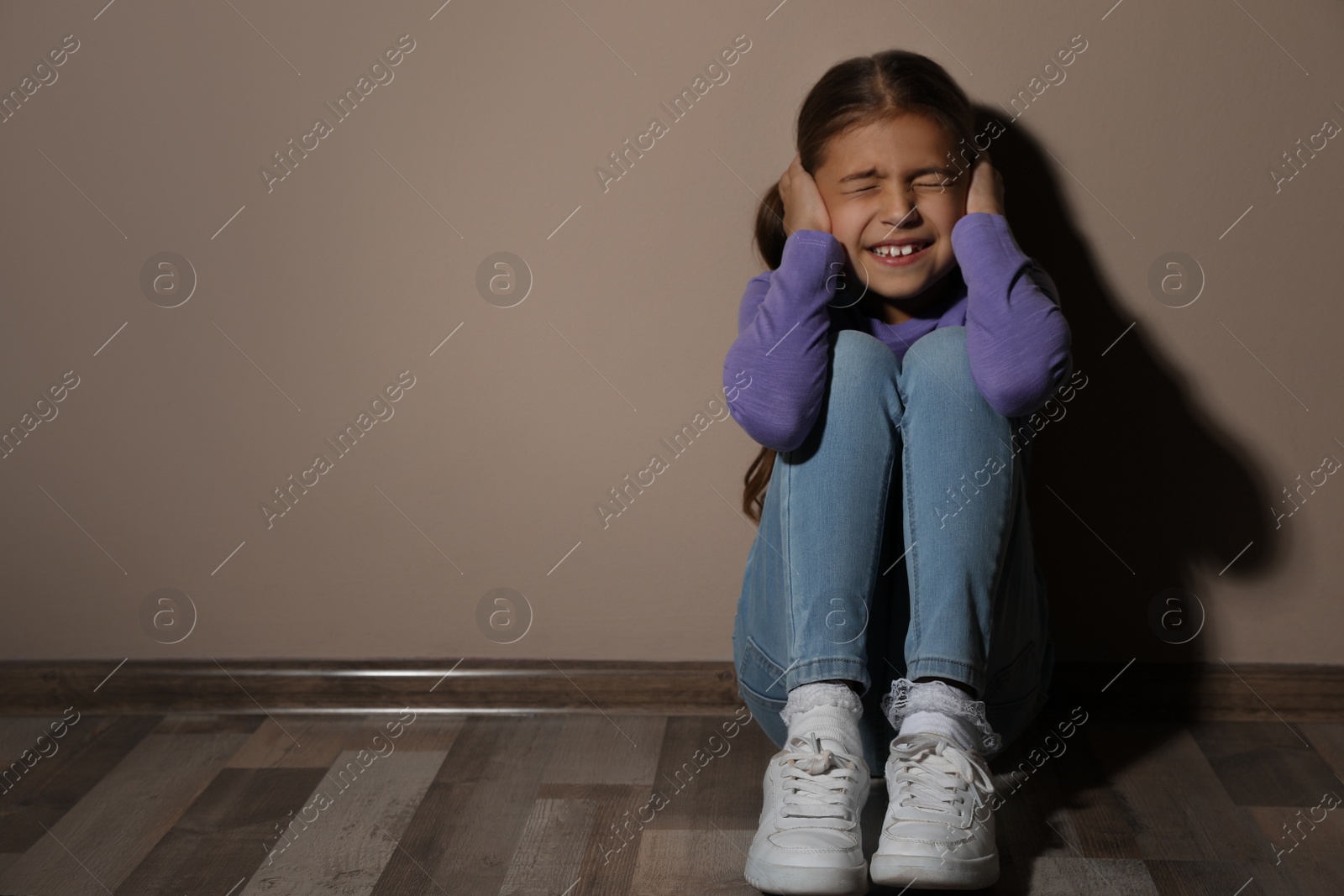 Photo of Scared little girl near beige wall, space for text. Domestic violence concept