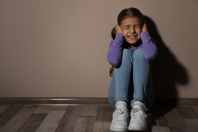 Scared little girl near beige wall, space for text. Domestic violence concept
