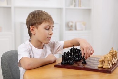 Cute little boy playing chess at table in room