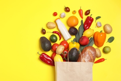Photo of Shopping paper bag with different groceries on yellow background, flat lay. Space for text
