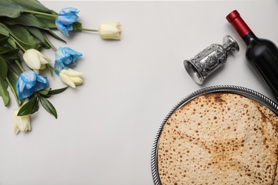 Photo of Tasty matzos, wine and tulips on light grey background, flat lay with space for text. Passover (Pesach) celebration