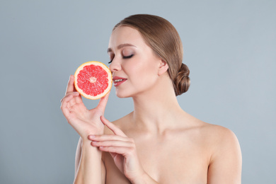 Young woman with cut grapefruit on grey background. Vitamin rich food