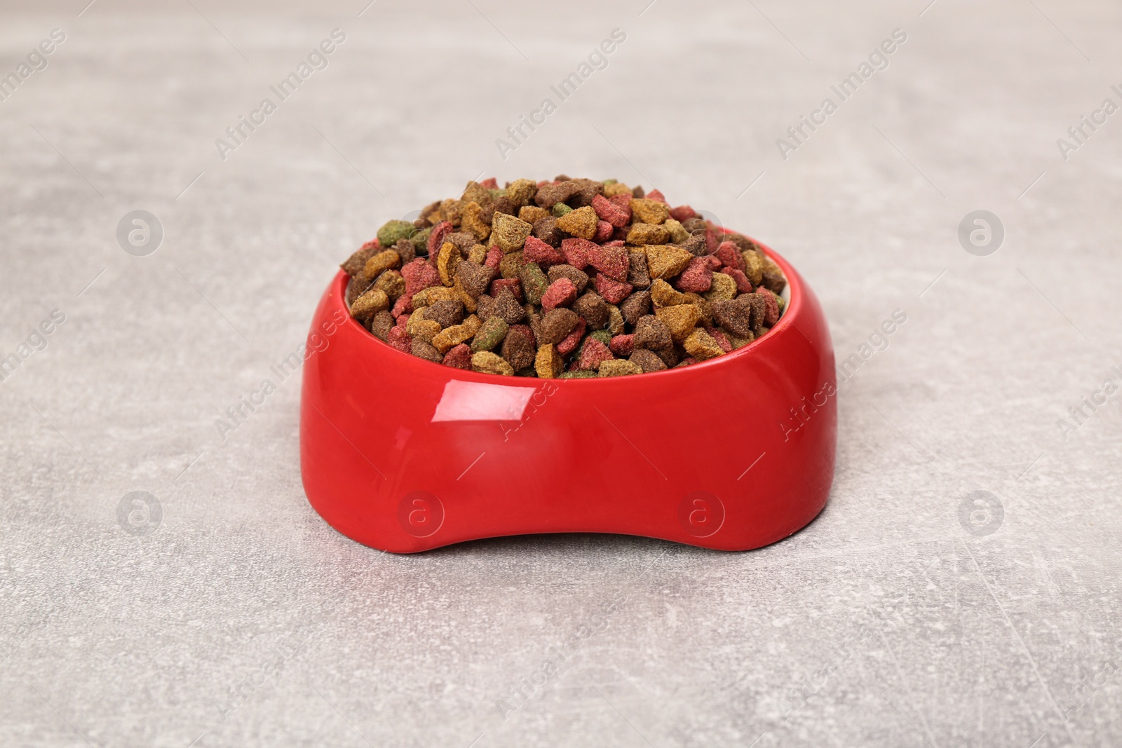 Photo of Dry cat food in red pet bowl on grey surface