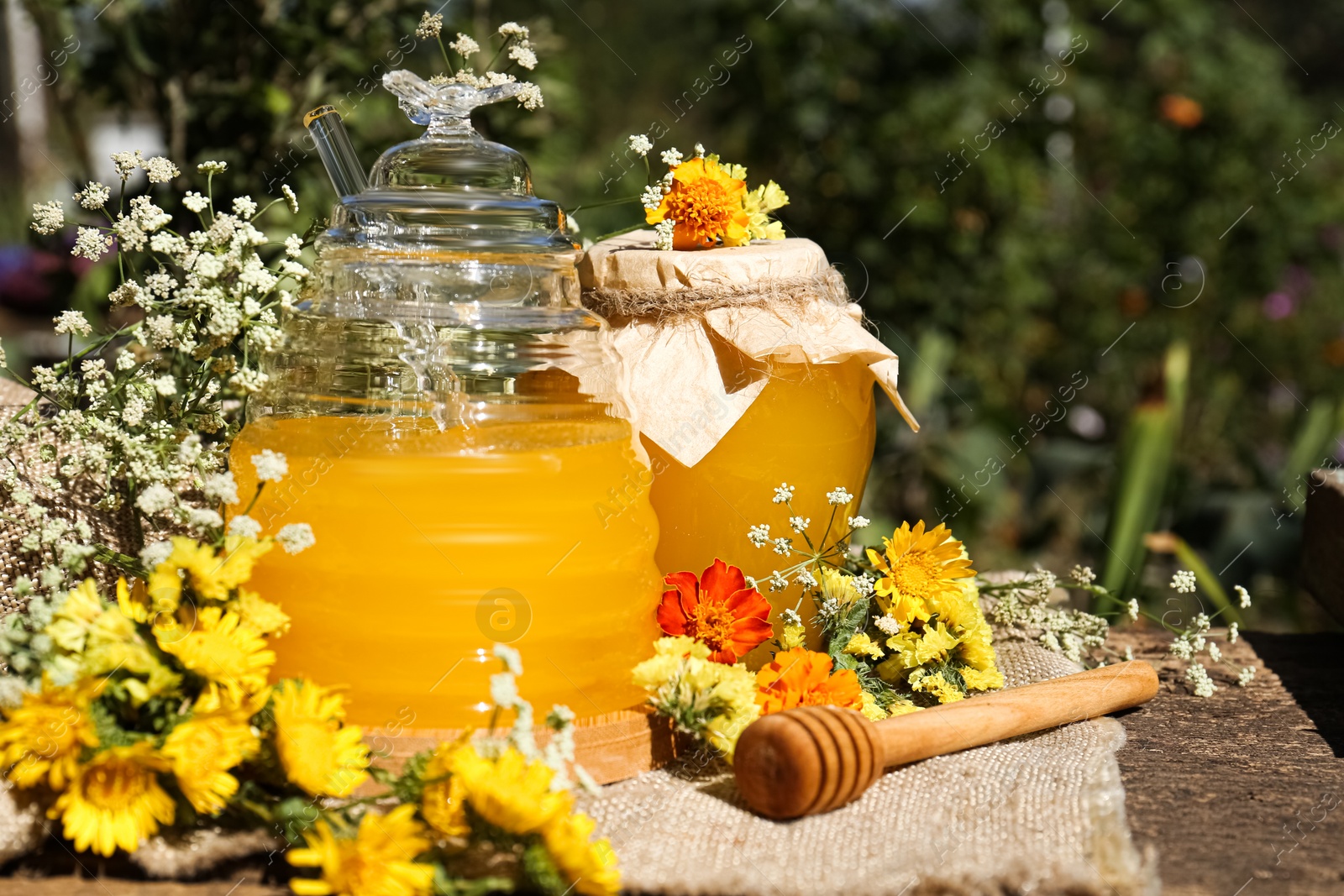 Photo of Delicious fresh honey and beautiful flowers on wooden table in garden