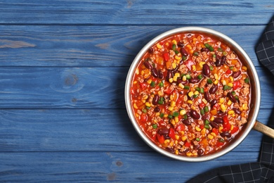 Photo of Frying pan with chili con carne on wooden background, top view. Space for text