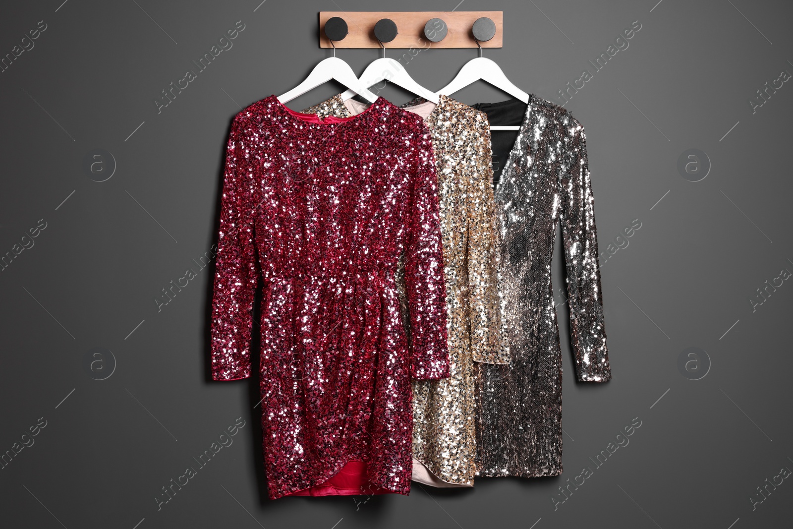 Photo of Different shiny beautiful women's party dresses on hangers near grey wall. Stylish trendy clothes for high school prom