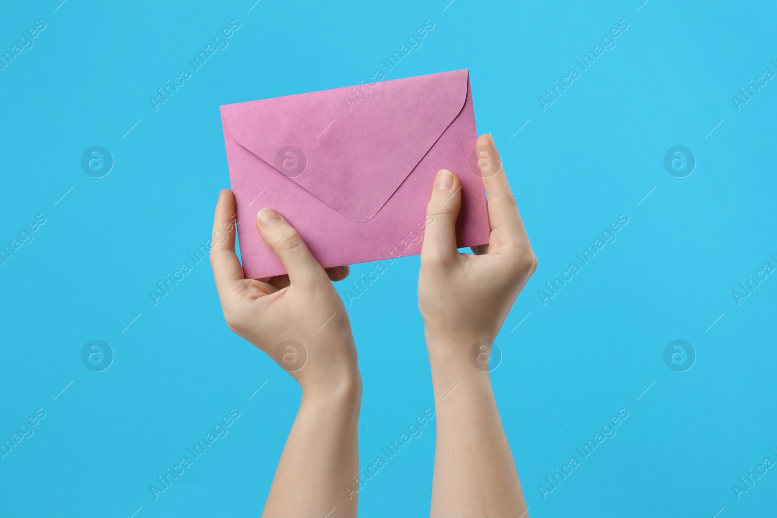 Photo of Woman holding pink paper envelope on light blue background, closeup