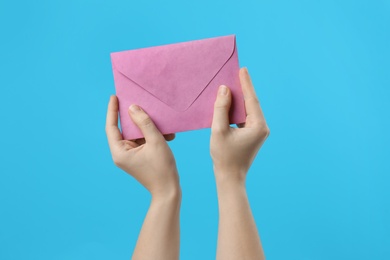 Woman holding pink paper envelope on light blue background, closeup