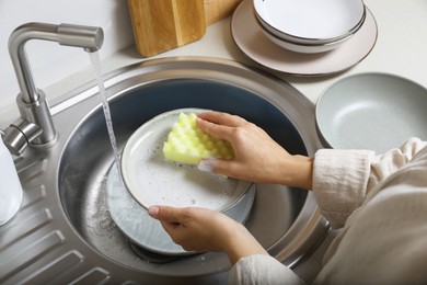 Photo of Woman washing plate in kitchen sink, above view