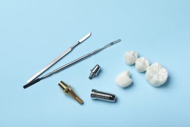 Parts of dental implant, bridge and medical tools on light blue background, flat lay
