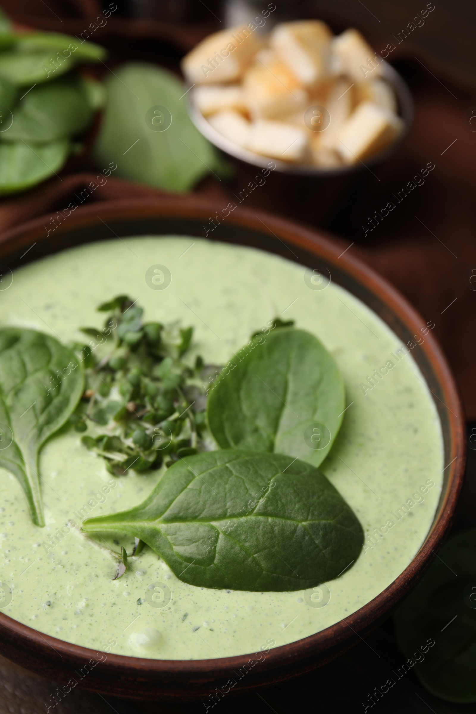 Photo of Delicious spinach cream soup with fresh leaves and microgreens in bowl on wooden table, closeup